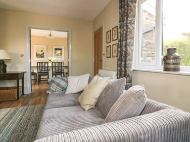 A living room with a gray sofa and pillows next to a window showing a dining area at Crantock Lodge in Crantock