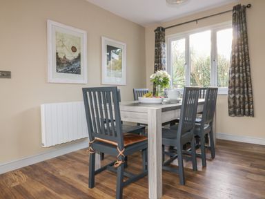 A dining room with a wooden table and six chairs by a window with curtains at Crantock Lodge in Crantock
