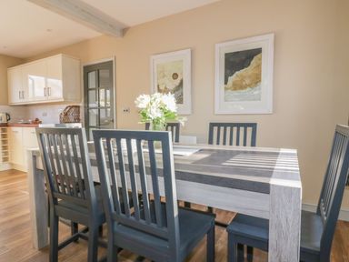 A dining table with six chairs and a vase with flowers in a kitchen with framed pictures on the wall at Crantock Lodge in Crantock