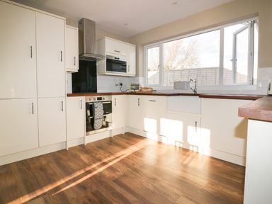 A kitchen with cream cabinets wooden countertops a stainless steel oven and hood a large window over a white sink at Crantock Lodge in Crantock