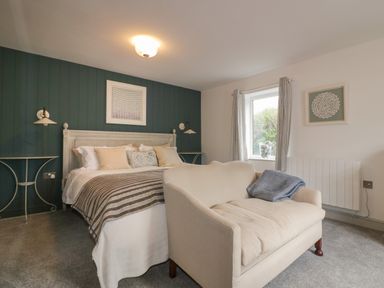A bedroom with a bed, beige loveseat, side tables, and a window at Crantock Lodge in Crantock