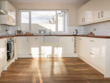 A kitchen with white cabinets wooden countertops a large window a toaster kettle bread and buns on the counter at Crantock Lodge in Crantock
