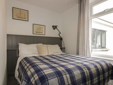 A bedroom with a bed covered with a checkered blanket and pillows a window with curtains and two framed ship pictures on the wall at Crantock Lodge in Crantock