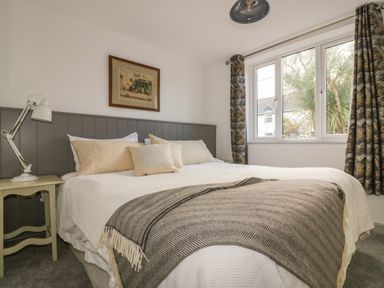 A bedroom with a bed, bedside table with a lamp, framed picture on the wall and window with curtains at Crantock Lodge in Crantock