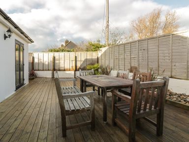 An outdoor wooden deck with a wooden table and chairs and a wooden fence surrounding at Crantock Lodge in Crantock