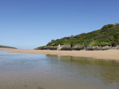 A sandy beach with a small body of water and shrub-covered rocky hill at Crantock Lodge in Crantock