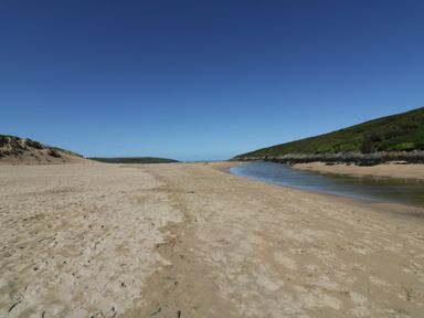 A sandy beach with a narrow river and grassy hills under a clear blue sky at Crantock Lodge in Crantock