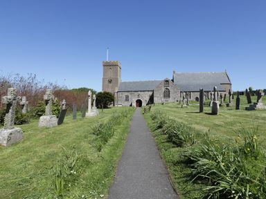 A stone church with a clock tower and surrounding gravestones at Crantock Lodge in Crantock