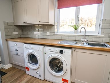 A kitchen laundry area with a washing machine dryer and sink under a window at Talarddu Cottage in Builth Wells