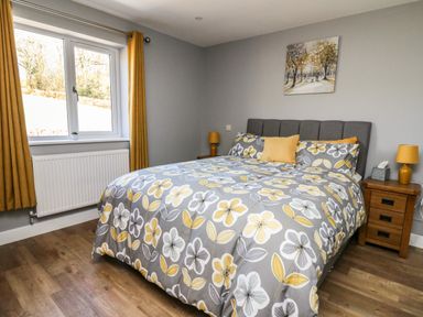 A bedroom with a bed with floral bedding wooden nightstands and yellow curtains at Talarddu Cottage in Builth Wells