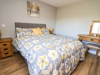 A bedroom with a double bed with floral bedding wooden bedside tables and a dressing table with a stool at Talarddu Cottage in Builth Wells