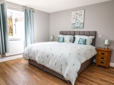 A bedroom with a double bed bedside table and window with curtains at Talarddu Cottage in Builth Wells