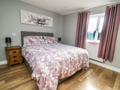 A bedroom with a double bed with floral bedding two bedside tables with lamps a window with curtains and a flower painting on the wall at Talarddu Cottage in Builth Wells
