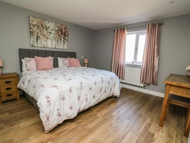 A bedroom with a double bed bedside tables a desk and pink curtains at Talarddu Cottage in Builth Wells