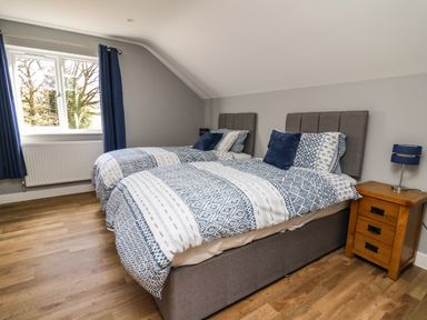 A bedroom with two beds side by side wooden nightstand and window with blue curtains at Talarddu Cottage in Builth Wells