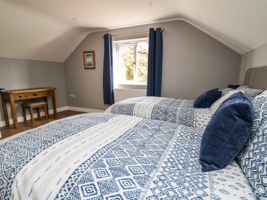 A bedroom with two beds a window with blue curtains a wooden desk and a small stool at Talarddu Cottage in Builth Wells