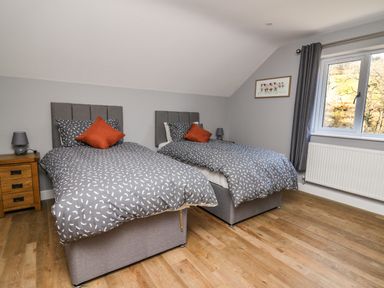 A bedroom with two single beds bedside tables lamps a window and a framed picture at Talarddu Cottage in Builth Wells