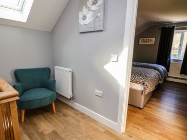 A hallway with a teal armchair and a radiator leading to a bedroom with two single beds at Talarddu Cottage in Builth Wells
