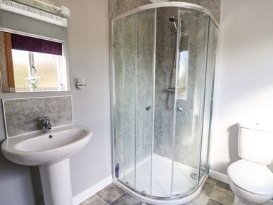 A bathroom with a glass shower enclosure a white sink and a white toilet at Talarddu Cottage in Builth Wells