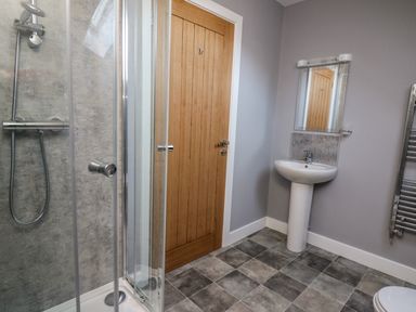A bathroom with a shower enclosure wooden door pedestal sink mirror and towel radiator at Talarddu Cottage in Builth Wells