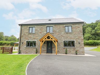 A stone house with wooden porch over the front door and paved driveway at Talarddu Cottage in Builth Wells