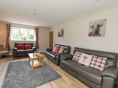 A living room with leather sofas wooden coffee table and animal paintings at Talarddu Cottage in Builth Wells
