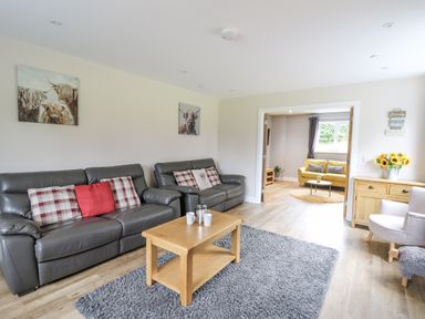 A living room with two black leather sofas a wooden coffee table and a grey rug at Talarddu Cottage in Builth Wells