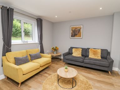 A living room with yellow and grey sofas a round coffee table on a rug and a window with curtains at Talarddu Cottage in Builth Wells