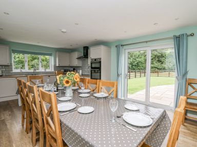 A dining area with a table set for eight and a kitchen with cabinets and appliances at Talarddu Cottage in Builth Wells