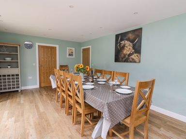 A dining room with a table set for eight with wooden chairs a gray polka dot tablecloth and sunflowers at Talarddu Cottage in Builth Wells
