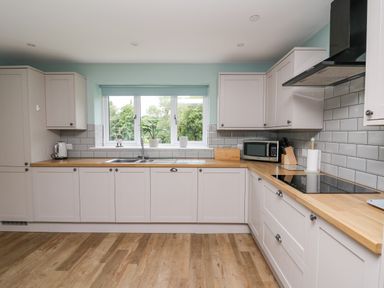 A kitchen with wooden countertops white cabinets a microwave toaster and a window with a plant on the sill at Talarddu Cottage in Builth Wells