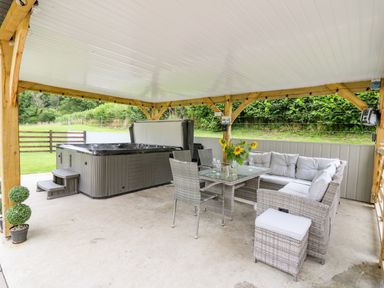 A covered outdoor seating area with wicker furniture a hot tub and a table with sunflowers at Talarddu Cottage in Builth Wells