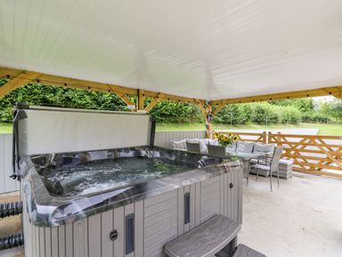 A covered outdoor area with a hot tub and a dining table with chairs and flowers at Talarddu Cottage in Builth Wells