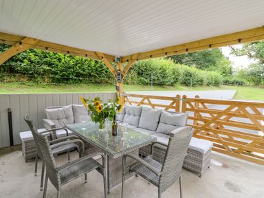 An outdoor covered seating area with a glass table sunflowers and wicker chairs at Talarddu Cottage in Builth Wells