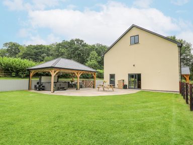A backyard with a wooden gazebo a picnic table and grass at Talarddu Cottage in Builth Wells