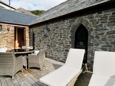 An outdoor patio with wicker chairs and a table next to a stone building with arched windows at Frogwell Chapel in Frogwell near Callington