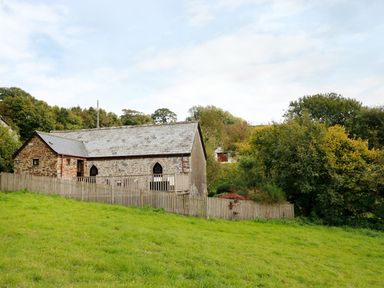 A stone building with a slate roof and wooden fence on a grassy slope surrounded by trees at Frogwell Chapel in Frogwell near Callington