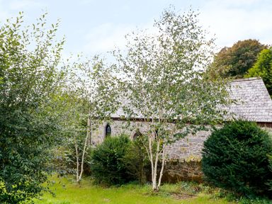 A stone building with arched windows surrounded by grass trees and bushes at Frogwell Chapel in Frogwell near Callington