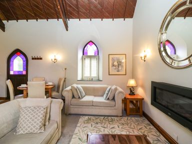 A living room with beige sofas a wooden coffee table a patterned rug wall lamps and a stained glass window at Frogwell Chapel in Frogwell near Callington