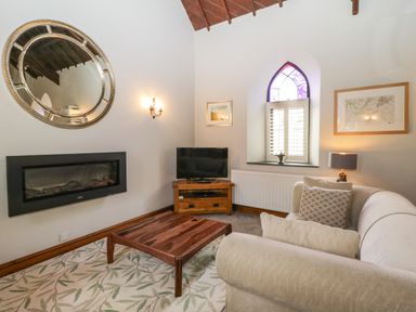 A living room with a beige sofa wooden coffee table wall-mounted fireplace and a corner TV at Frogwell Chapel in Frogwell near Callington