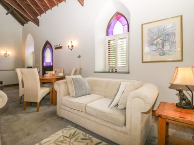 A living room with a beige sofa and dining table with chairs near stained glass windows at Frogwell Chapel in Frogwell near Callington