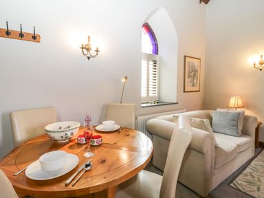 A dining table with chairs and tableware next to a window and a sofa with cushions in a living area at Frogwell Chapel in Frogwell near Callington