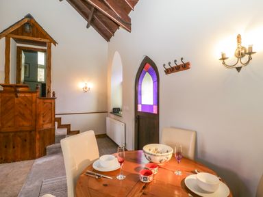 A dining area with a wooden table set with bowls cups and glasses near a stained glass door and stairs at Frogwell Chapel in Frogwell near Callington