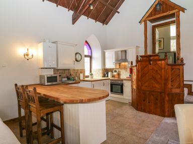 A kitchen with wooden countertops white cabinets a microwave and two wooden chairs at Frogwell Chapel in Frogwell near Callington