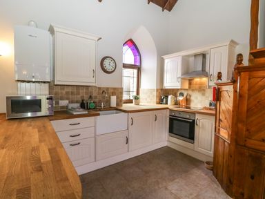 A kitchen with wooden countertops white cabinets a microwave a stove and an arched window at Frogwell Chapel in Frogwell near Callington