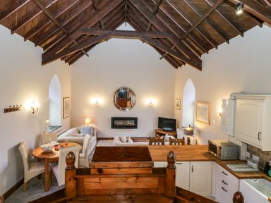 A living room and kitchen area with wooden ceiling beams and a round dining table at Frogwell Chapel in Frogwell near Callington