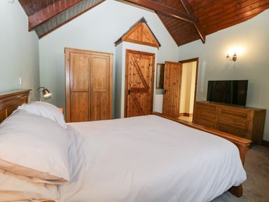 A bedroom with a bed white bedding wooden wardrobe wooden doors and a wooden dresser with a television at Frogwell Chapel Frogwell near Callington