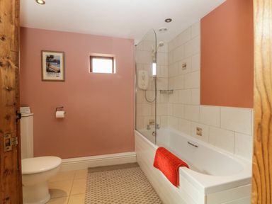 A bathroom with a white bathtub shower combo with a red towel and a toilet on a tiled floor at Frogwell Chapel in Frogwell near Callington