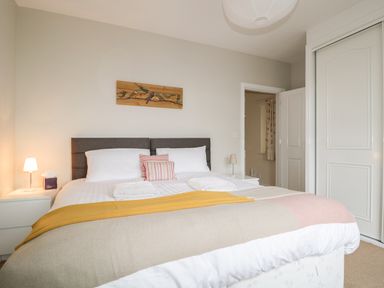 A bedroom with a double bed with pillows and folded towels and bedside tables with lamps at Limhus Cottage in Keswick