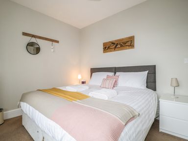 A bedroom with a double bed white and pink bedding bedside tables with lamps and wall decorations at Limhus Cottage in Keswick